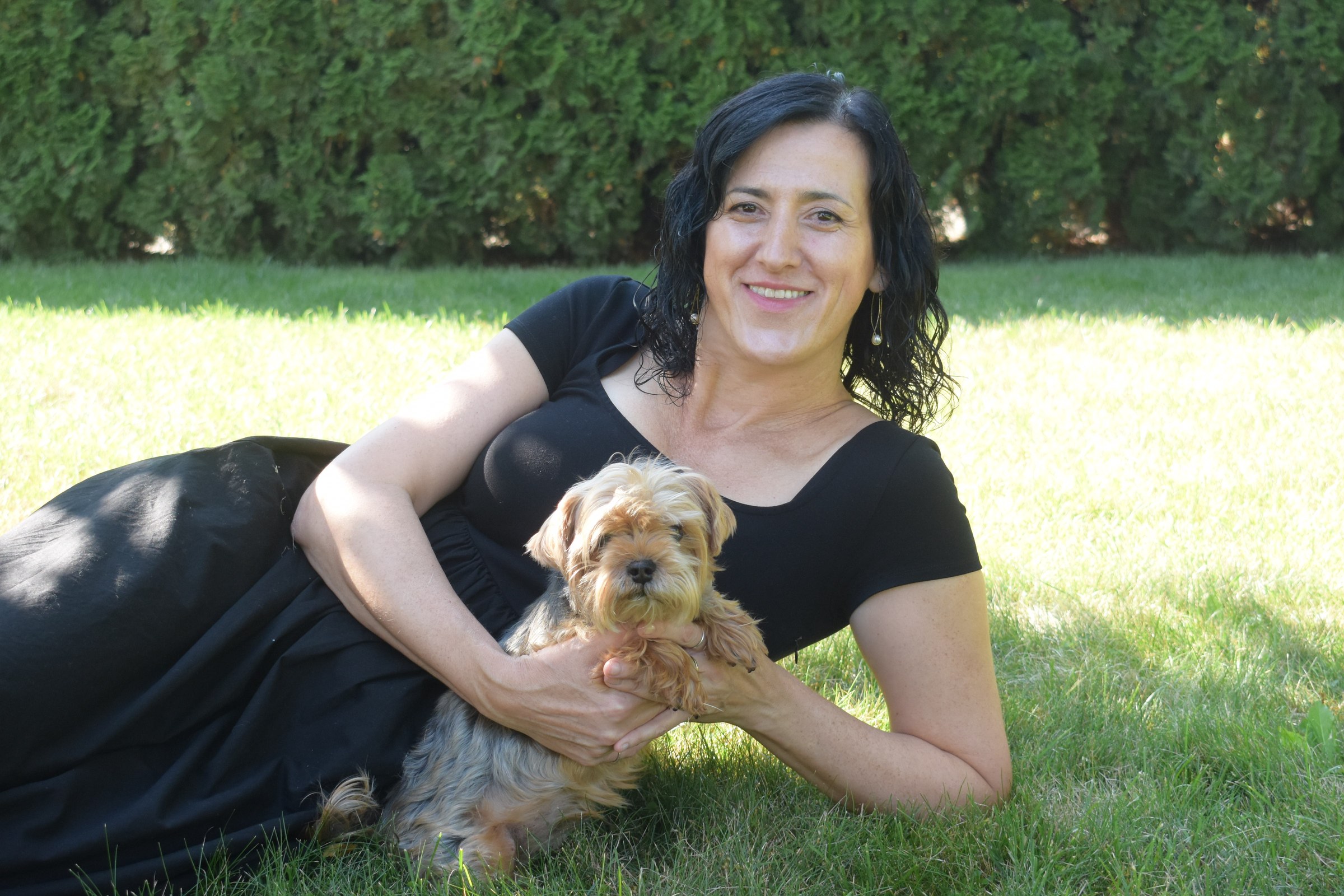 Lejla lying outdoors on the grass, smiling, holding her dog